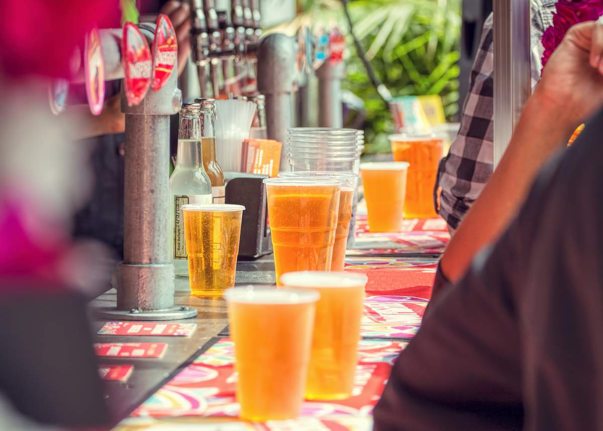 Beer and people at outdoor bar. Plastic cups of beer and cider at an outdoor bar in summer with people drinking.