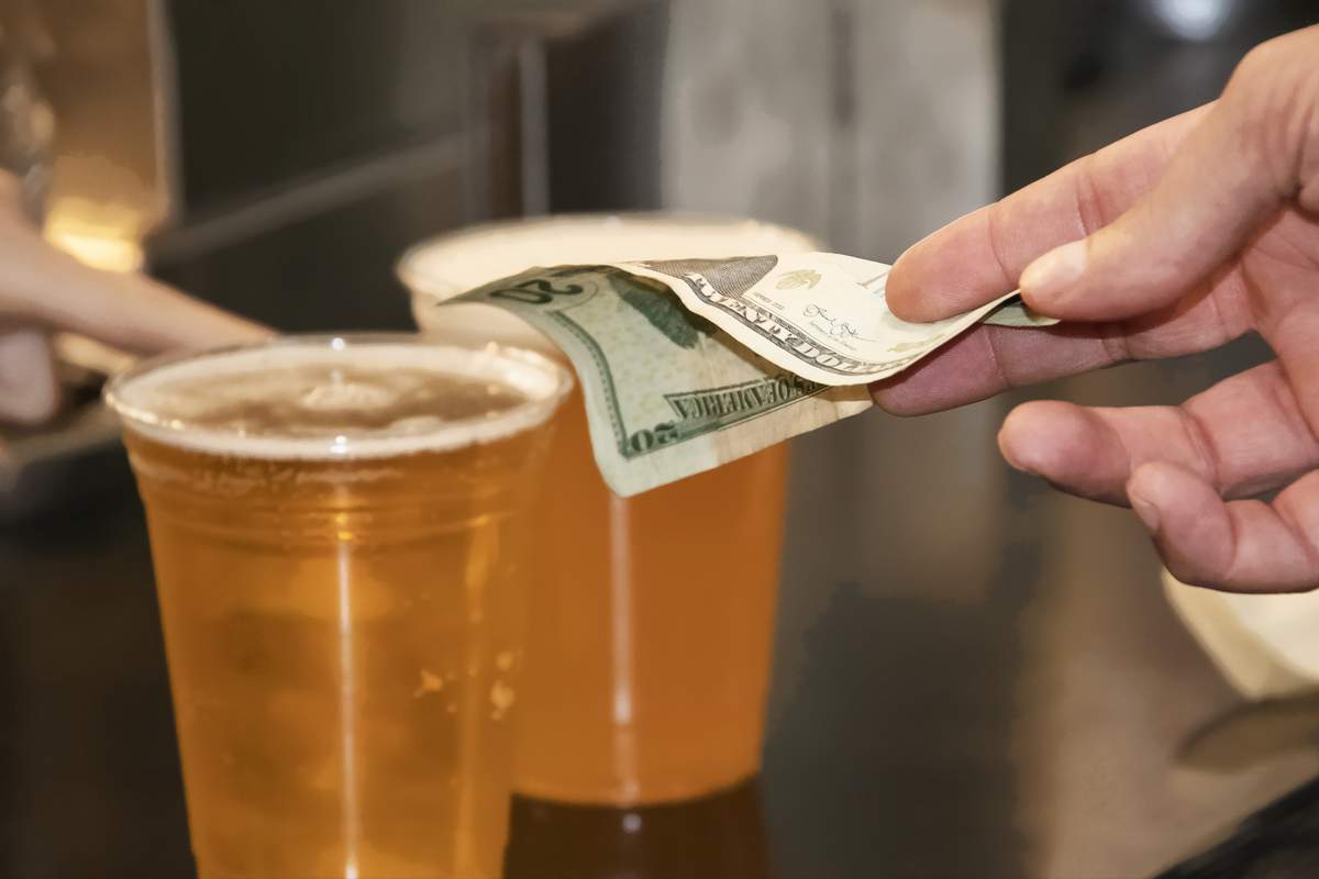 Mans hand paying for two plastic cups of beer with a USD twenty dollar bill.