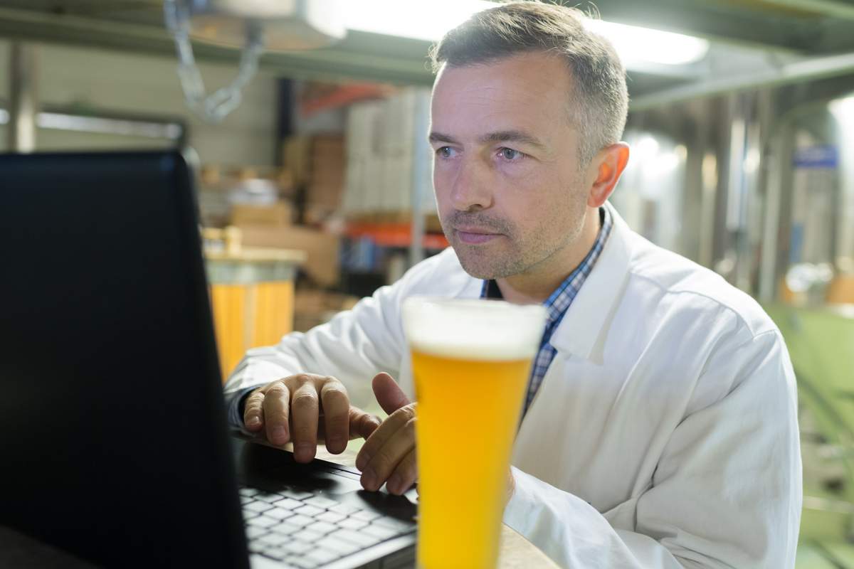 brewer beer pro looking at computer webinar with beer in brewery