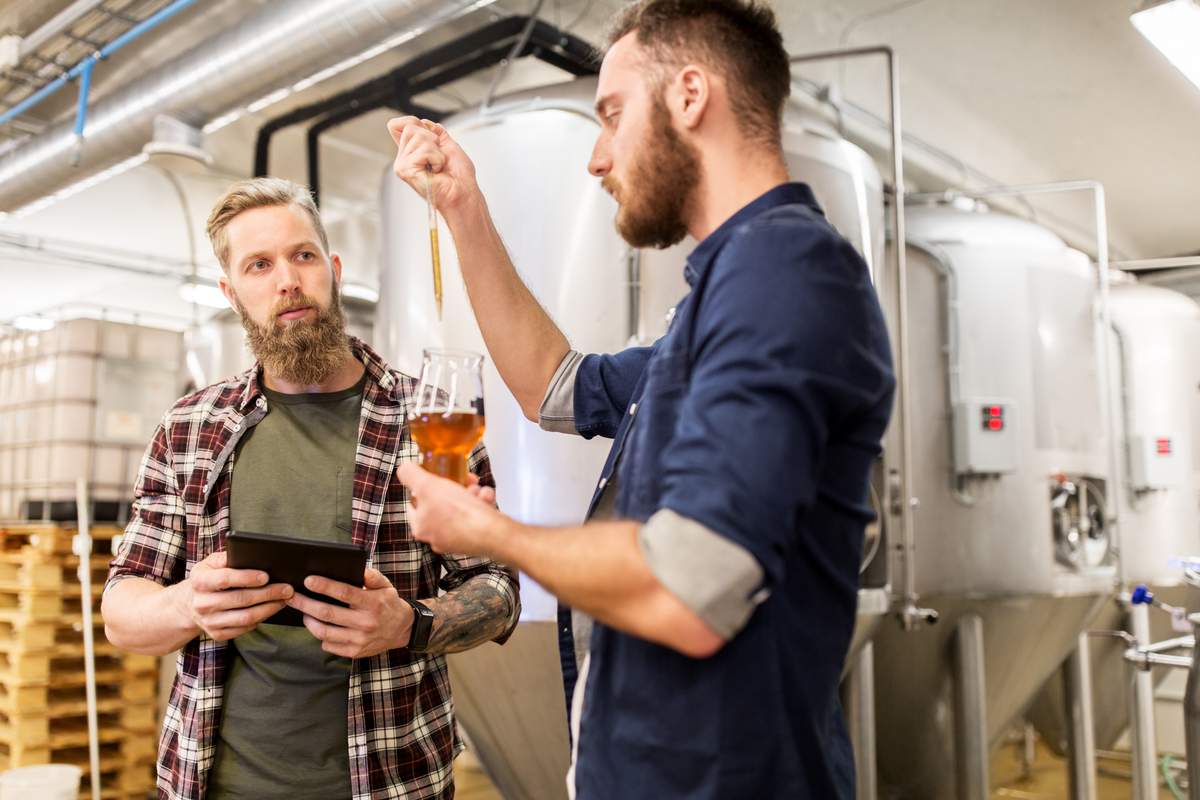 brewers talking in the brewhouse using lab equipment to test beer quality control 